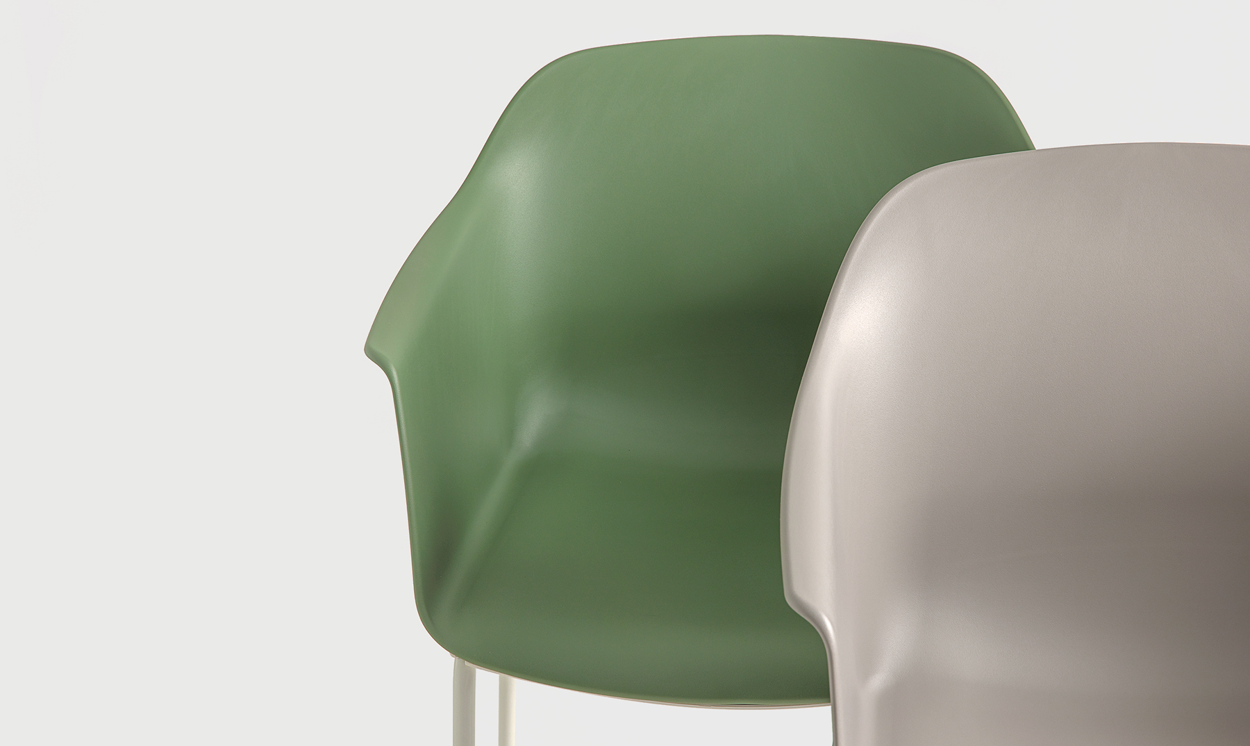 The image shows a front view of two Noom 60 chairs designed by Alegre Design for Actiu. One chair is light gray, and the other is green. Both chairs feature a smooth, curved bucket-style seat with integrated armrests and a minimalist design.