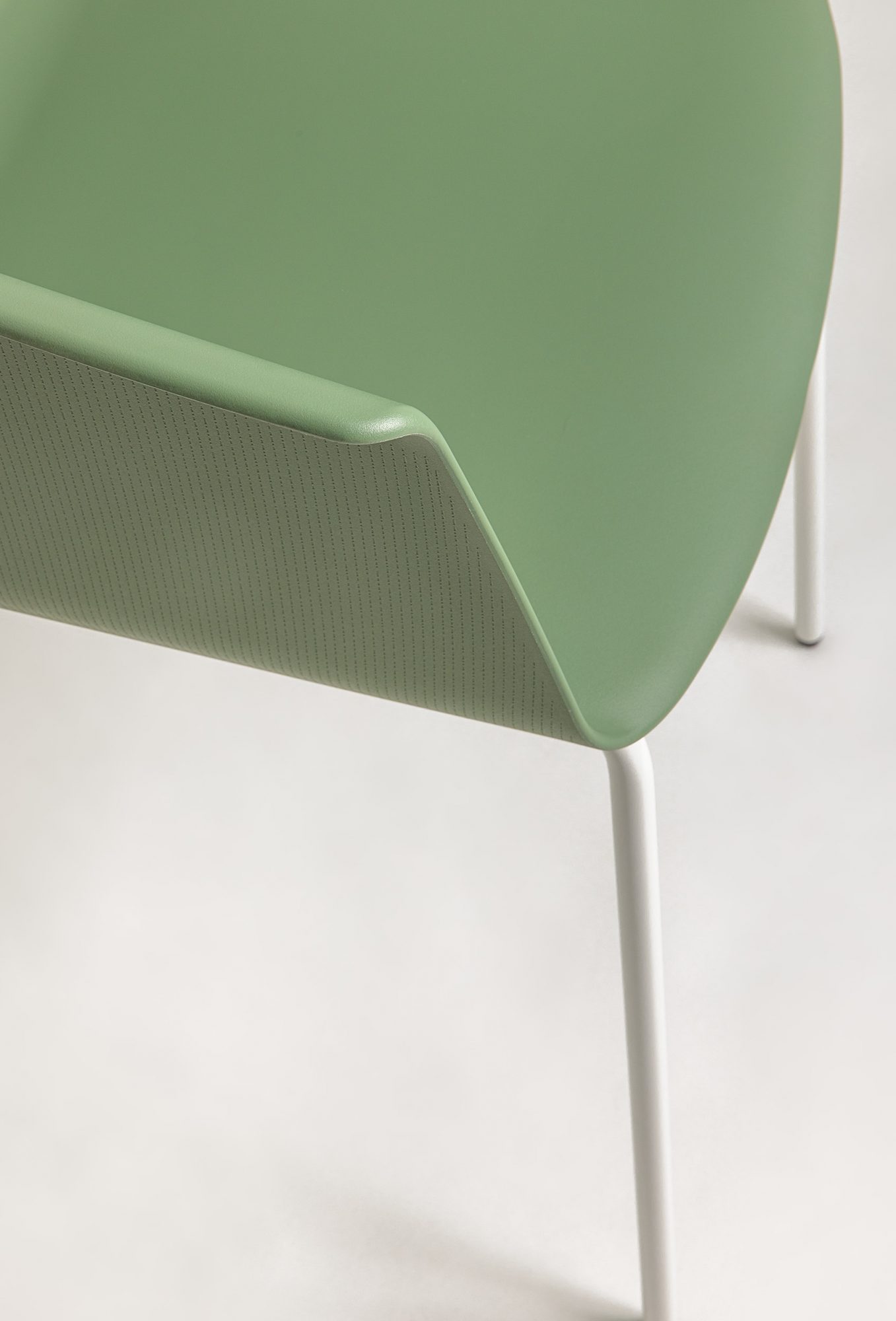 Detailed close-up of the armrest of the Noom 60 chair designed by Alegre Design for Actiu. The chair features a smooth, olive green surface with a subtle, fine-textured pattern. The white metal legs are partially visible, emphasizing the chair's minimalist and modern design.