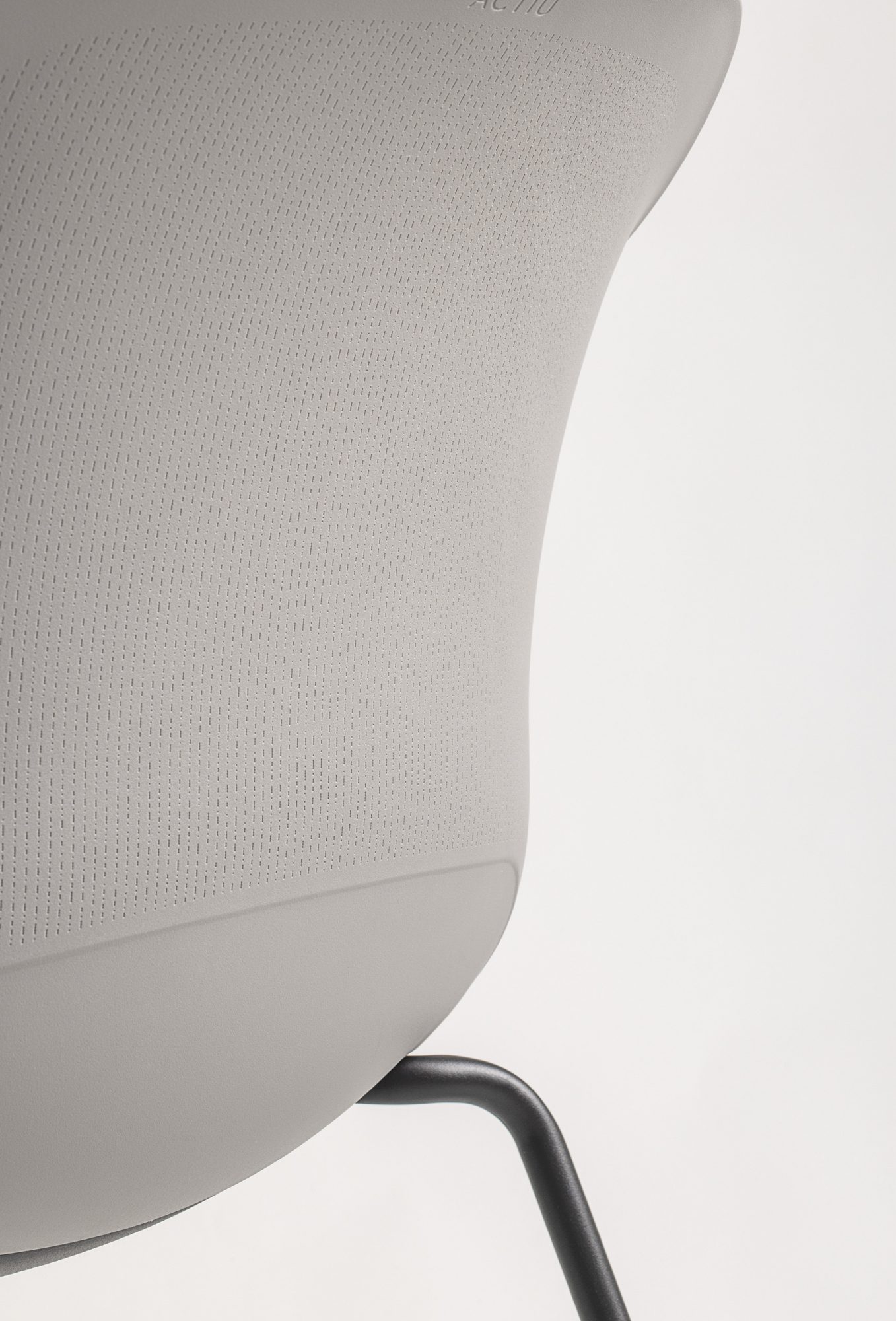 The image shows a detailed close-up of the back texture of the Noom 60 chair designed by Alegre Design for Actiu. The chair features a smooth, light gray surface with a subtle, fine-textured pattern. The black metal legs are partially visible, emphasizing the chair's minimalist and modern design.