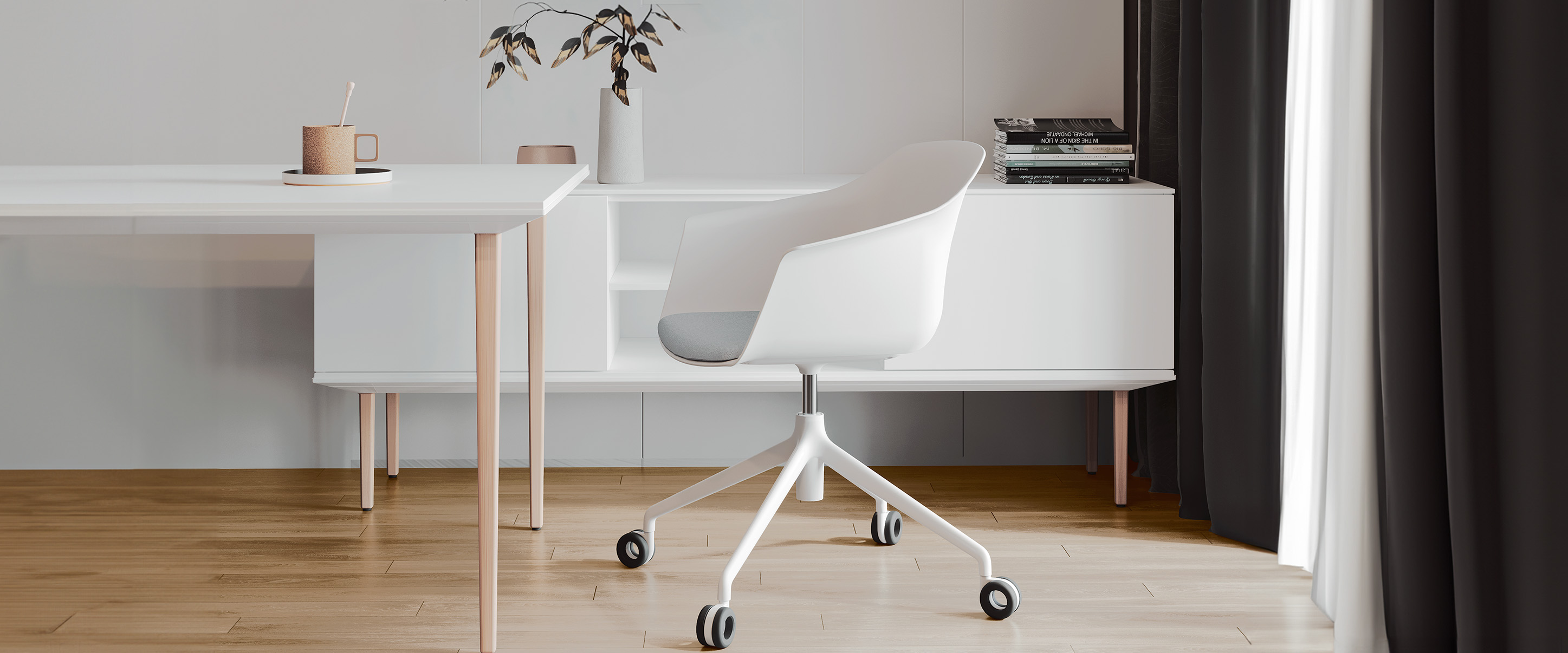 The image shows a modern, minimalist office setting featuring a white Noom 60 chair designed by Alegre Design for Actiu. The chair has a curved, bucket-style seat with integrated armrests and is mounted on a white, wheeled base for mobility. The scene includes a white desk, a sideboard, and some decorative items like a cup, a vase with branches, and stacked books. The overall design is sleek and contemporary, ideal for a clean and organized workspace.