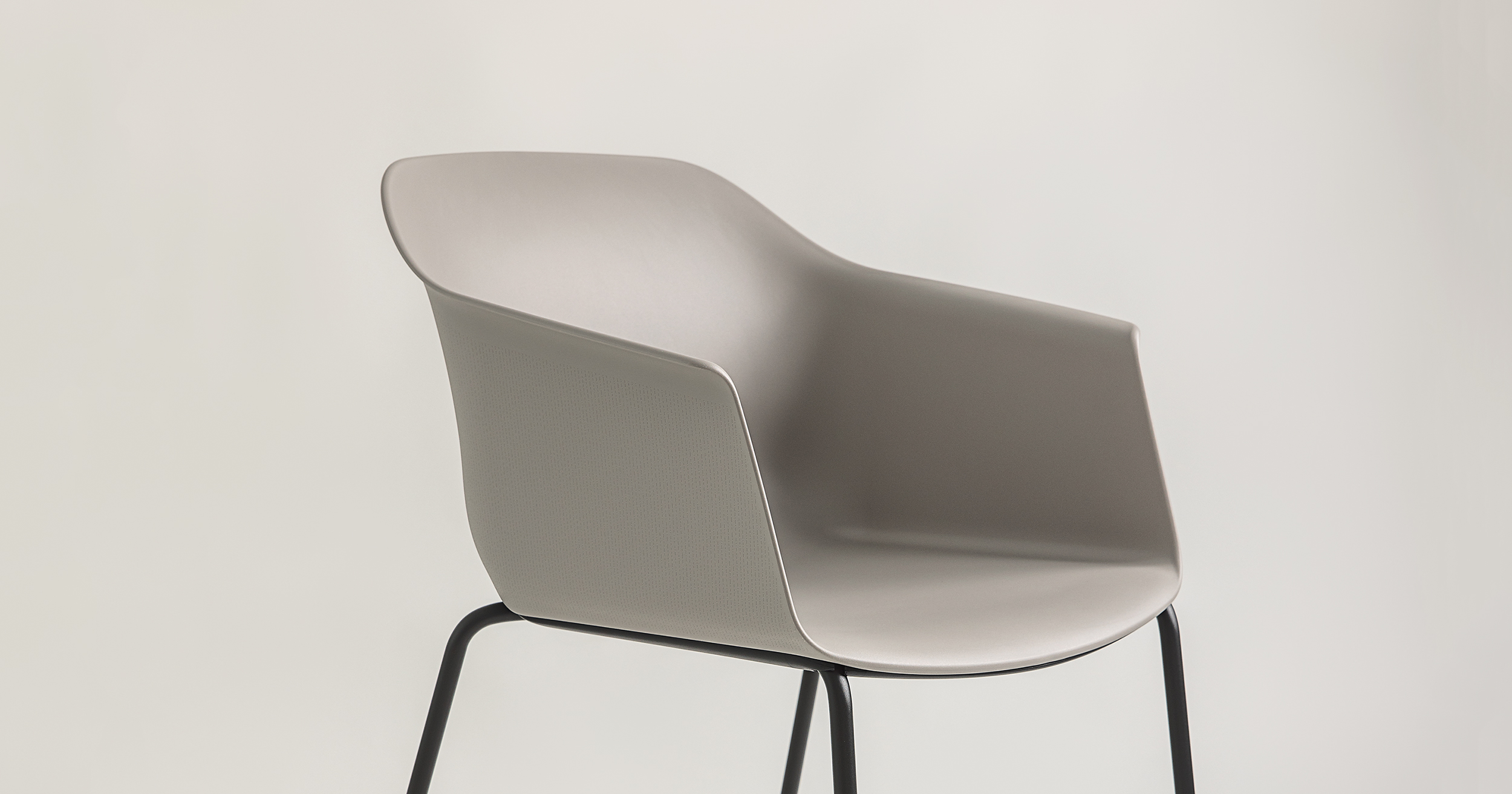A modern, minimalist chair named Noom 60 designed by Alegre Design for Actiu. The chair features a curved, bucket-style seat in a smooth, light gray color. It has thin, black metal legs and integrated armrests. This sleek and contemporary chair is suitable for various settings such as offices or homes.