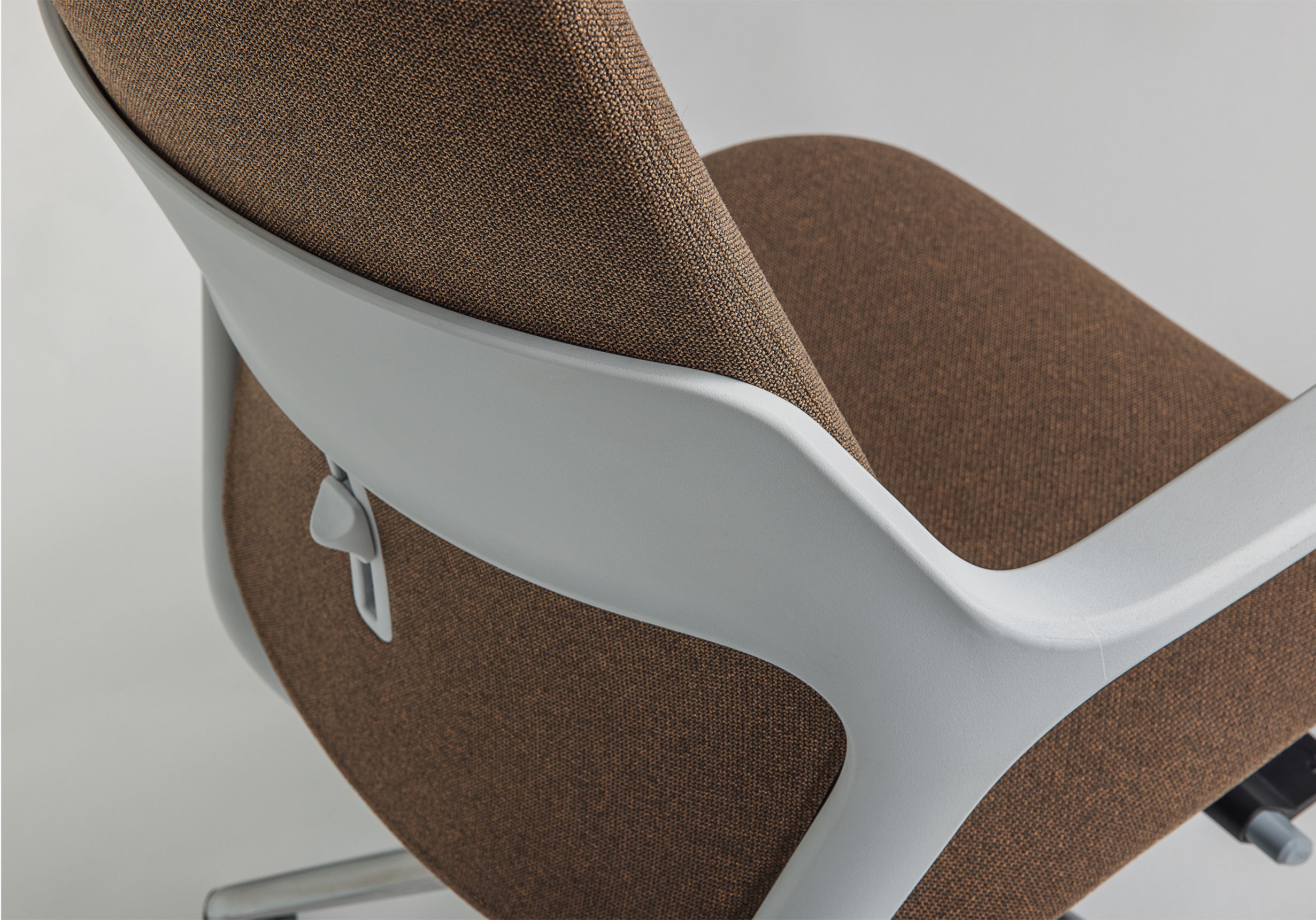 Close-up of the back of an OFY chair in brown, designed by Alegre Design for Narbutas. The image highlights the ergonomic thermoplastic backrest and the button for adjustable lumbar support, ideal for enhancing comfort in hybrid and modern workspaces.